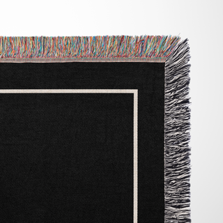 Custom cotton throw blanket with black background and colorful fringe and a white ribbon on a light gray background from The Blanket Shop