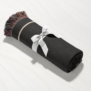 Rolled up custom throw blanket with black background and colorful fringe and a white ribbon on a light gray background from The Blanket Shop