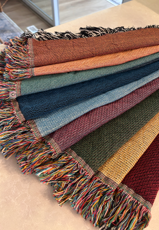 Selection of custom woven throw blankets with fringes in various colors on a neutral background