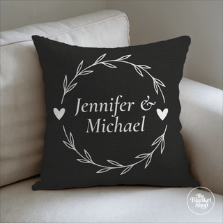 Black pillow with 'Jennifer & Michael' text on a beige couch and The Blanket Shop Logo