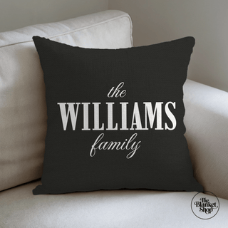 Black pillow with 'the WILLIAMS Family' text on a beige couch and The Blanket Shop Logo