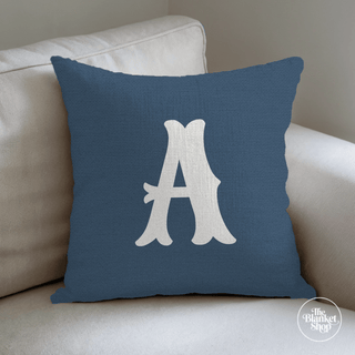 Blue pillow with A monogram text on a beige couch and The Blanket Shop Logo
