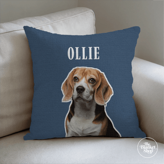 Blue pillow with a dog's face and name 'Ollie' on a beige couch and The Blanket Shop Logo