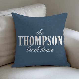 Blue pillow with 'the THOMPSON beach house' text on a beige couch and The Blanket Shop Logo