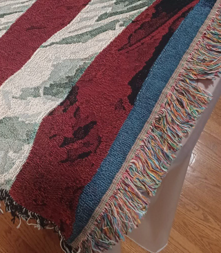 Close-up of a colorful woven blanket with fringes on a wooden floor.