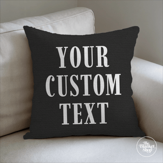 Custom black throw pillow with 'Your Custom Text' on a beige couch and The Blanket Shop Logo