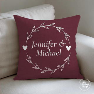 Maroon pillow with 'Jennifer & Michael' text on a beige couch with The Blanket Shop Logo