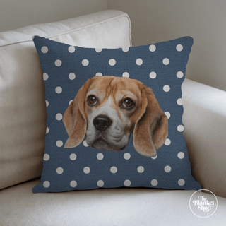 Pillow with a dog illustration on a blue polka dot background, placed on a beige couch with The Blanket Shop Logo