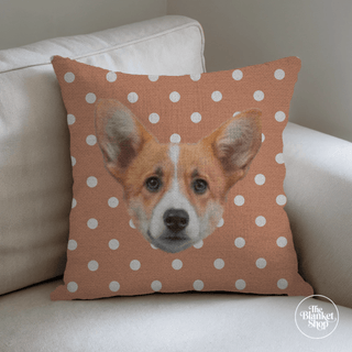 Pillow with a dog illustration on a orange polka dot background, placed on a beige couch with The Blanket Shop Logo