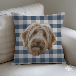 Pillow with a dog's face on a blue and white checkered pattern, placed on a beige couch with The Blanket Shop Logo