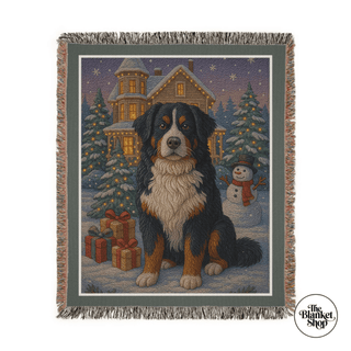 Woven blanket with a dog and Christmas scene design, featuring a house, trees, and snowman with The Blanket Shop Logo