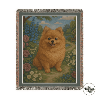 Woven blanket with a dog design featuring a Pomeranian in a garden setting, branded 'The Blanket Shop'.